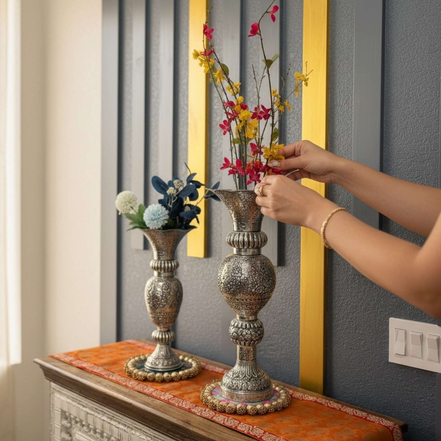 Person arranging flowers in ornate vases on a decorative table.
