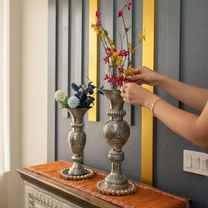 Person arranging flowers in ornate vases on a decorative table.