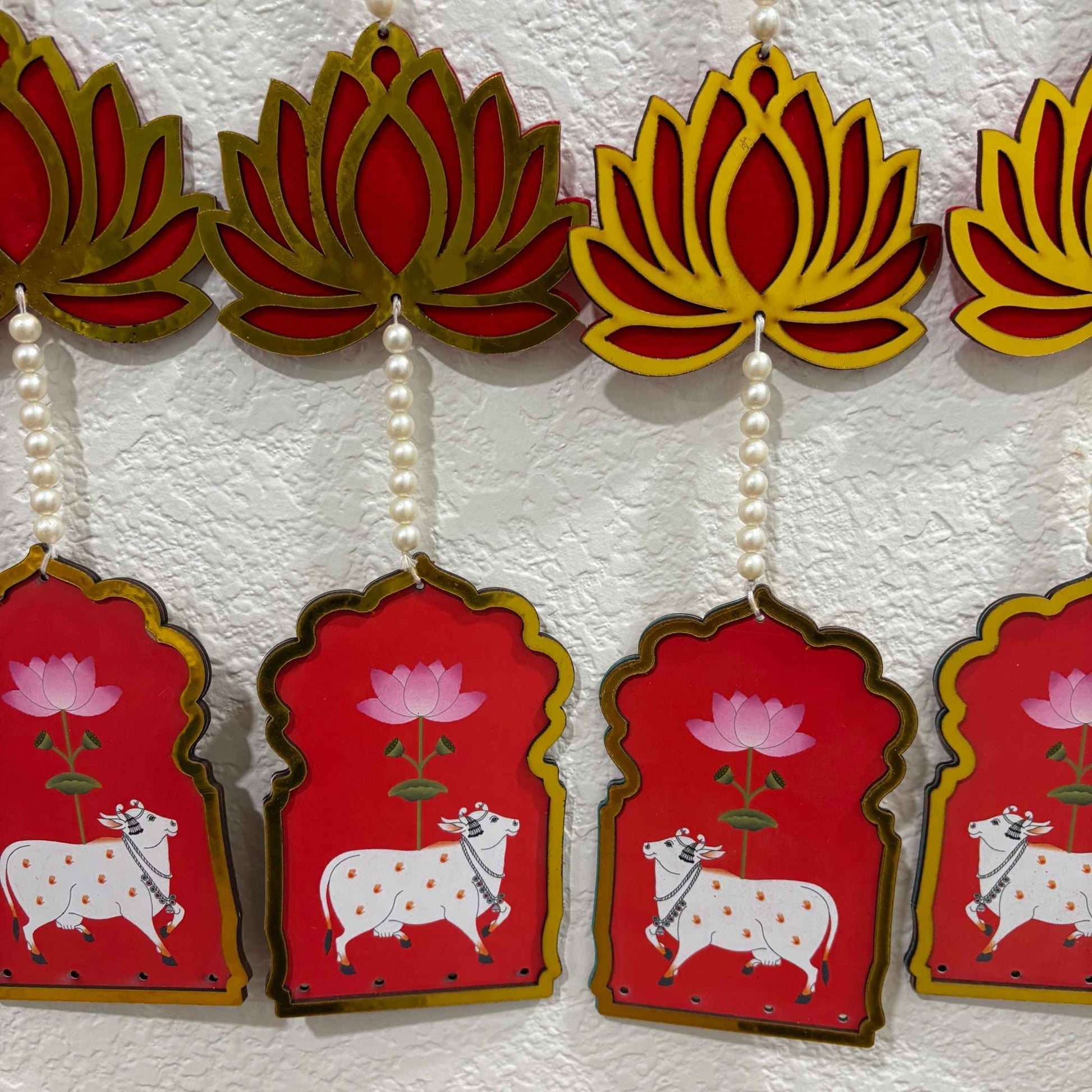 Decorative hanging with red and gold lotus designs and white cows on a textured white background