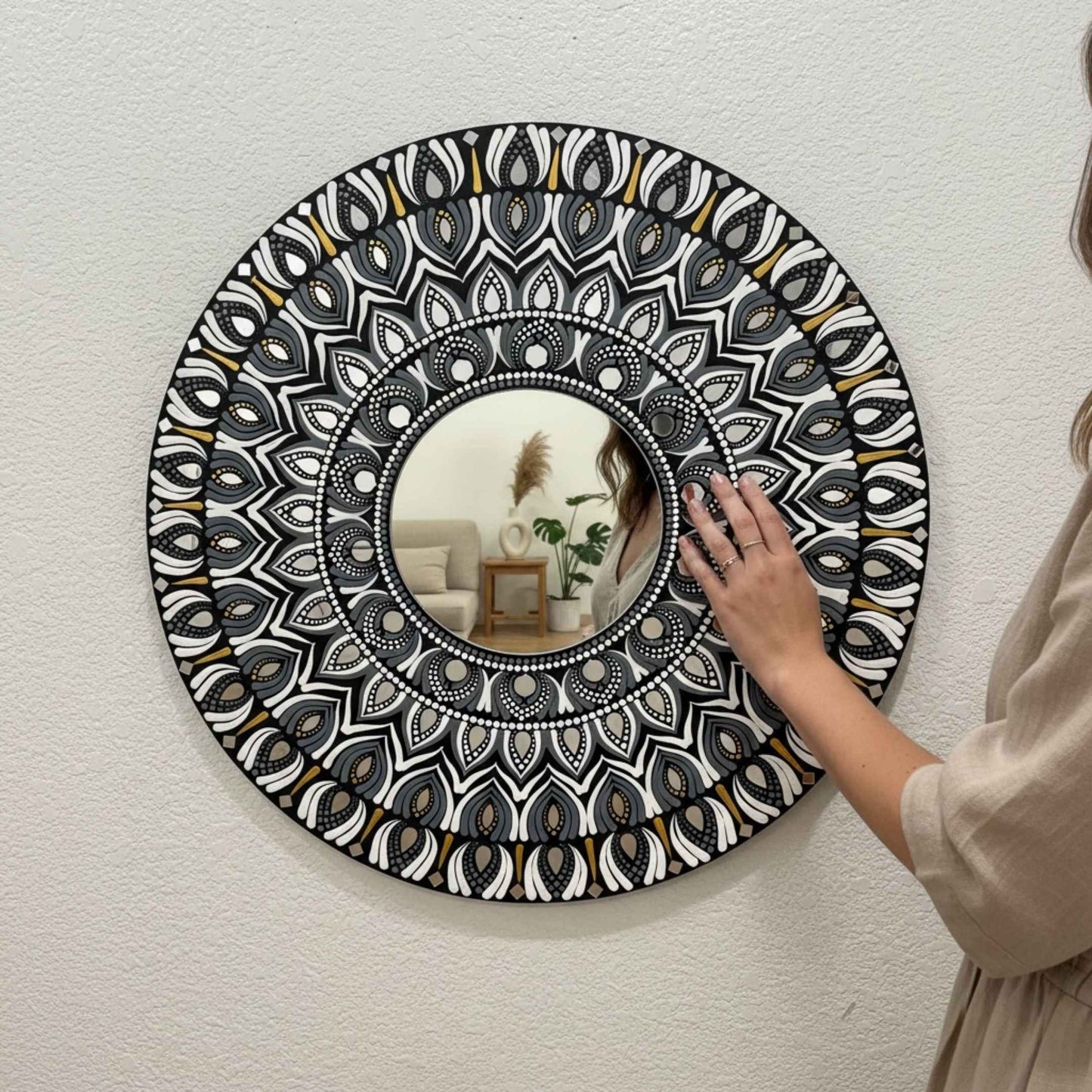 Person adjusting a mandala wall mirror with intricate black and white pattern
