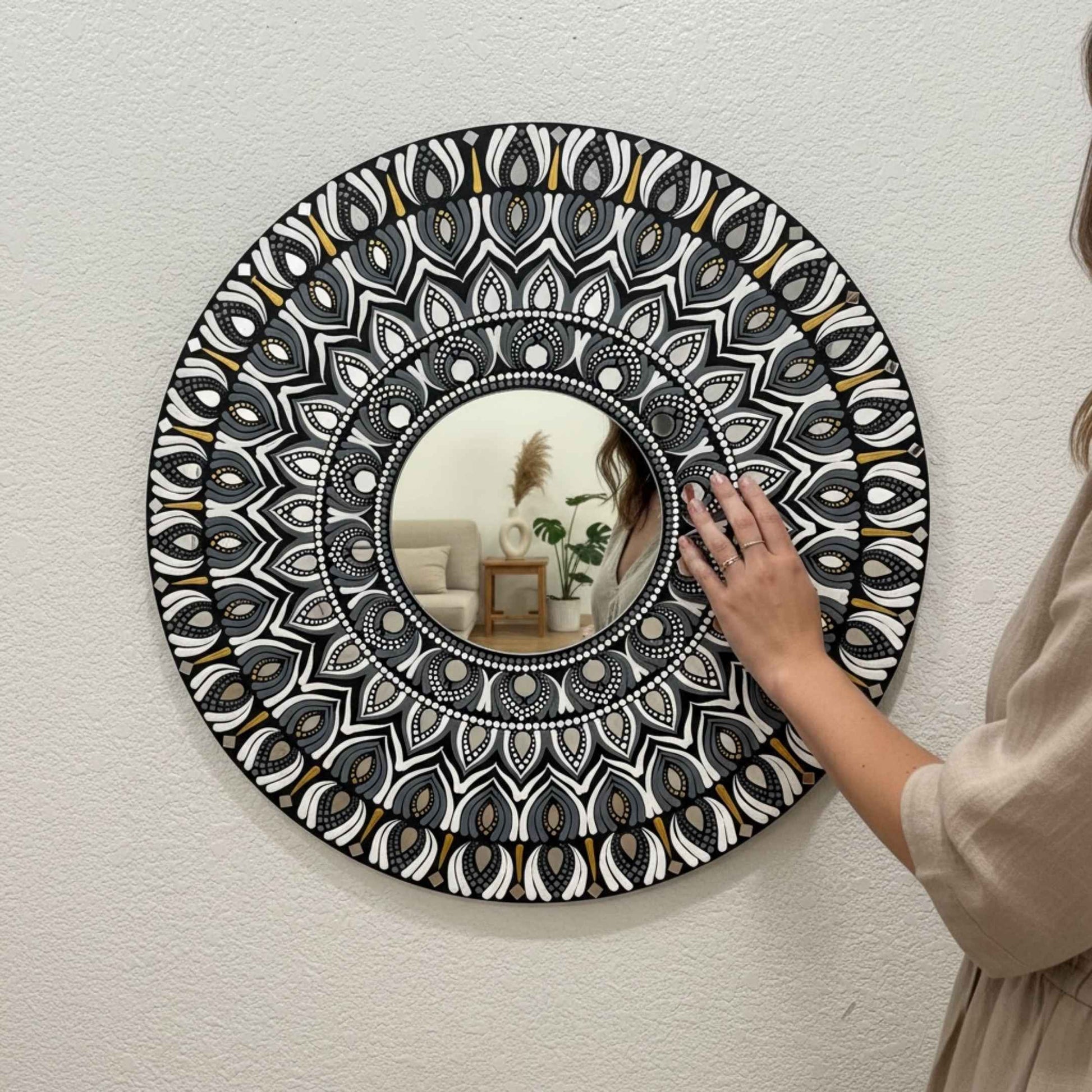 Person adjusting a mandala wall mirror with intricate black and white pattern