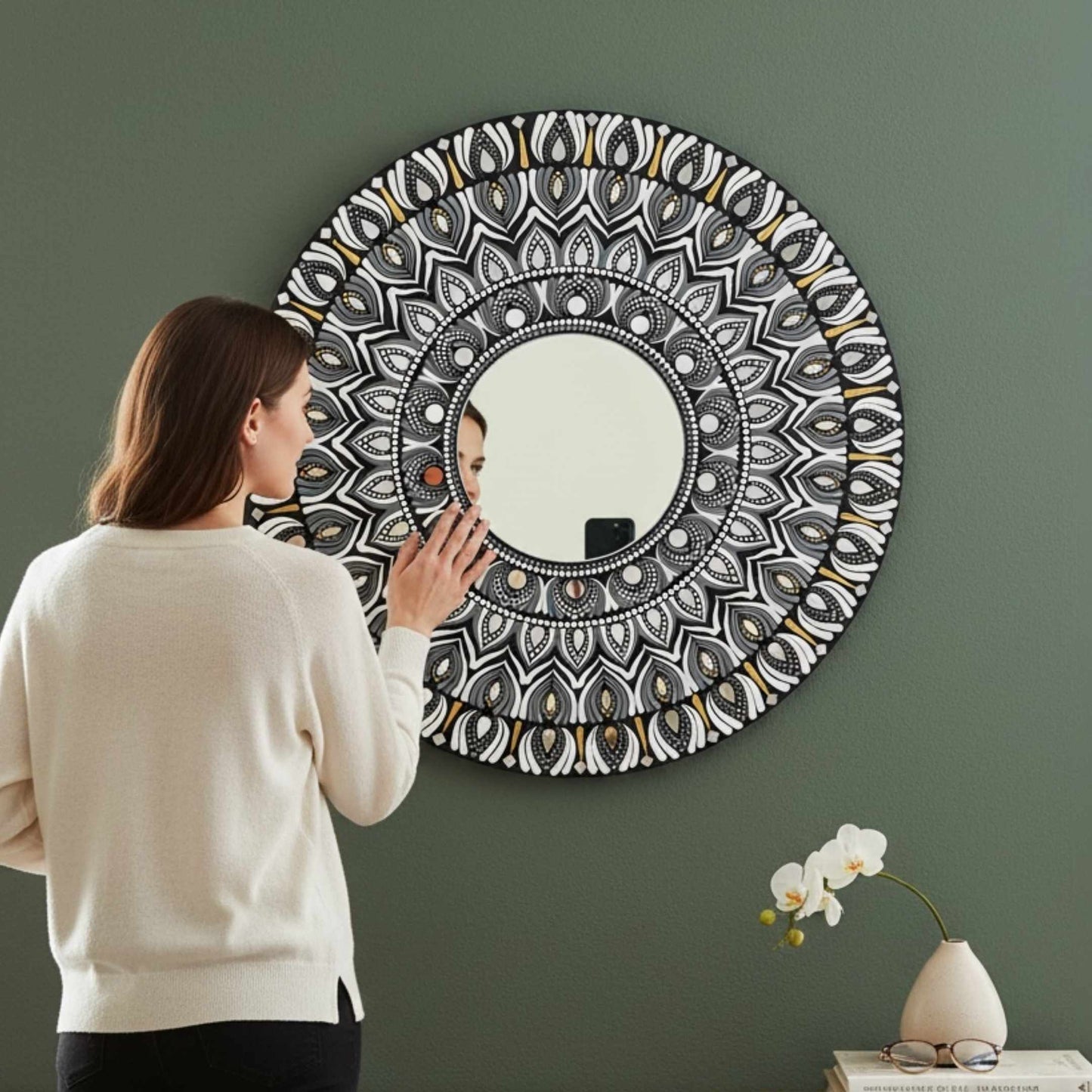 Woman looking at a round mandala wall mirror with intricate patterns on a green wall.
