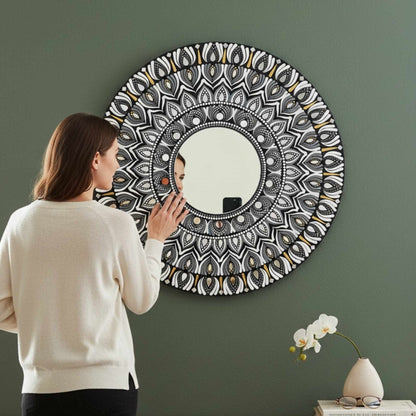 Woman looking at a round mandala wall mirror with intricate patterns on a green wall.