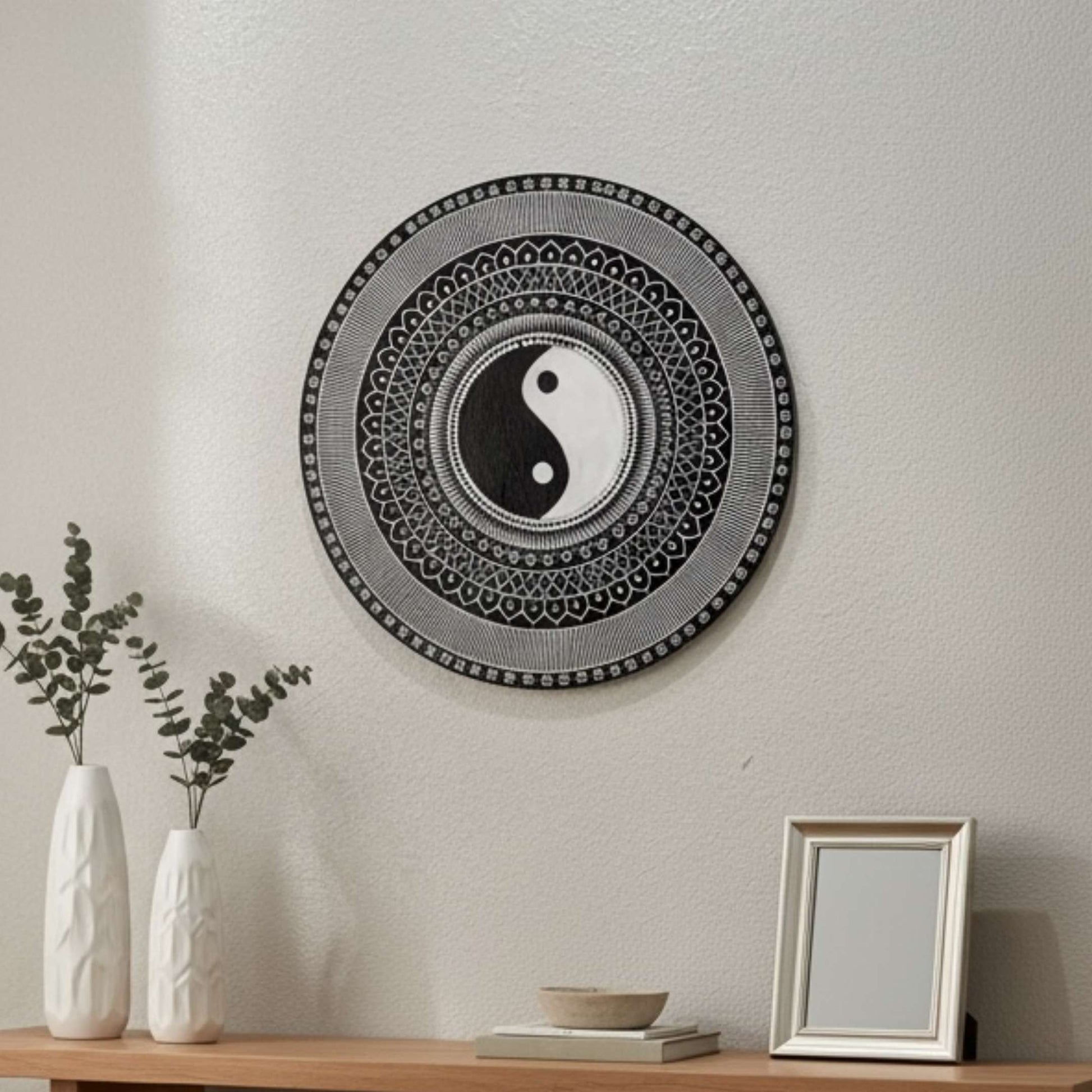 Yin Yang wall art on a plain wall with vases and a frame on a table.